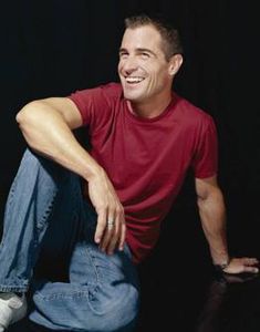 a man sitting on the ground with his legs crossed and smiling at the camera,