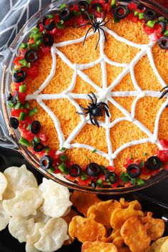 a spider web cake is decorated with cheese, black olives, and red peppers