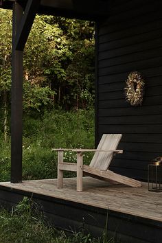 a wooden chair sitting on top of a wooden deck next to a black building with trees in the background