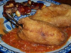 two fried food items on a blue and white plate with sauce, breaded meat and vegetables