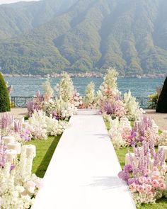 a long white aisle with flowers and greenery in front of a body of water