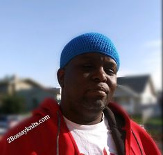 a man wearing a blue hat and red jacket in front of a street with houses