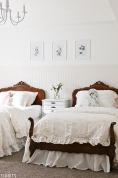 two twin beds in a white bedroom with chandelier and pictures on the wall