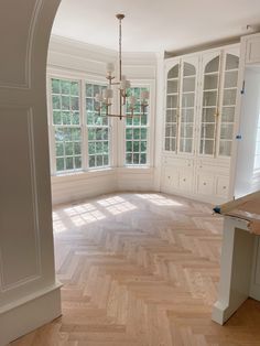 an empty kitchen with white cabinets and wood flooring in front of a large window