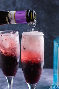 two wine glasses filled with red and pink liquid being poured into one glass by a bottle