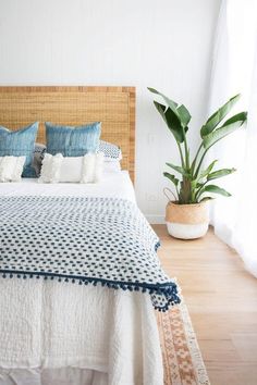 a bed with blue and white pillows on top of it next to a potted plant