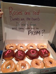 a box filled with lots of donuts next to a sign that says, roses are red donuts are the bomb do me not know and come with me to prom?