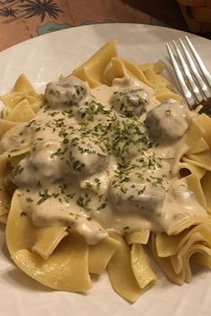 a white plate topped with pasta covered in sauce and meatballs next to a fork