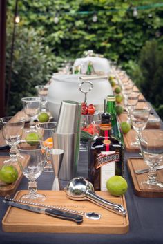 a long table is set with glasses, bottles and utensils for an outdoor party