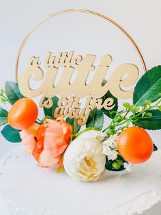 a white cake topped with an orange and white flower arrangement next to a wooden sign