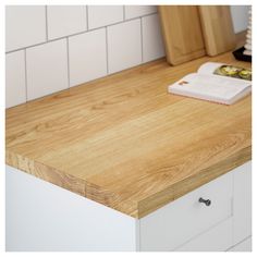 a wooden counter top in a kitchen next to a white tile backsplash with a book on it