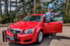 a man standing next to a red car with its door open and the driver leaning on it