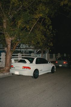 a white car parked in front of a tree at night