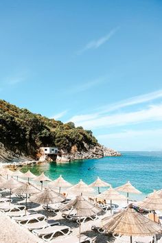 many umbrellas are set up on the beach near the blue water and hills in the background