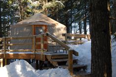 a yurt in the woods with snow on the ground and stairs leading up to it