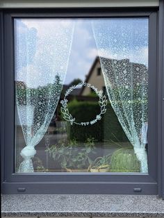 an open window with a wreath drawn on it's side and the reflection of a house in the window