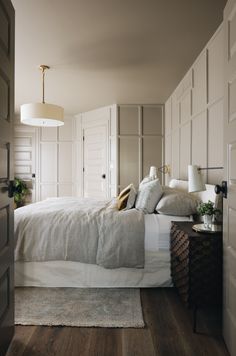 a white bed sitting in a bedroom next to a lamp and wooden floored walls