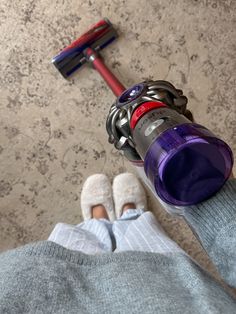 a person standing next to a purple and red cordless vacuum cleaner on the floor