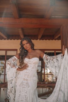 a woman in a white wedding dress standing on a porch with her arms around her body