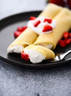 a plate topped with crepes covered in whipped cream and strawberries next to a fork