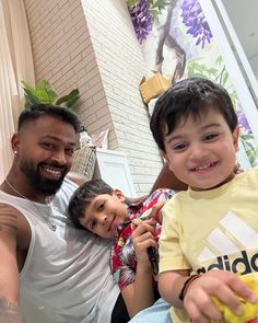 a man and two children are sitting on a couch smiling at the camera while one child holds a banana in his hand