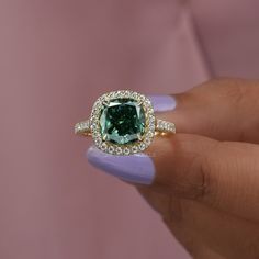 a woman's hand holding a ring with a green diamond in the center and white diamonds around it