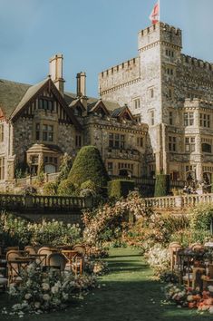 an old castle like building with lots of flowers in the foreground and tables set up outside