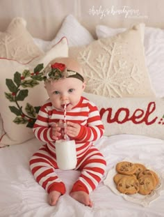 a baby sitting on a bed with cookies and milk in front of her, holding a straw