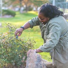 a woman is tending to some plants in the garden with rocks and grass behind her