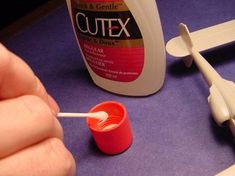 a hand holding a toothbrush next to a bottle of glue and an airplane model