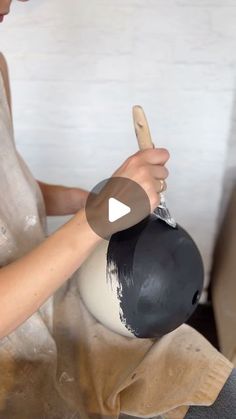 a woman is using a cell phone to paint a vase with black and white paint