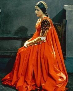 a woman in an orange dress is sitting on a chair and looking off to the side