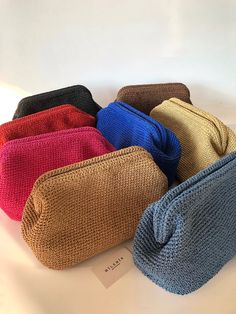 four different colored knitted bags sitting on top of a white table next to each other