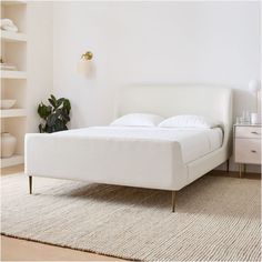 a white bed sitting on top of a wooden floor next to a wall mounted shelf