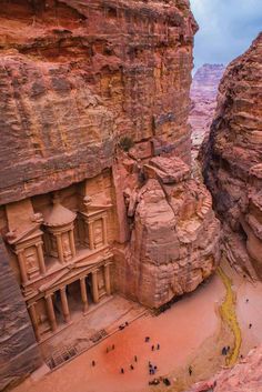 people are walking around in the desert near some large rocks and rock formations that look like they have been built into the side of a cliff