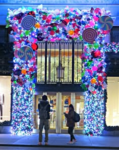 two people standing in front of a building decorated with christmas lights