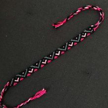 a pink and black braided lanyard sitting on top of a black cloth covered floor