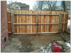 a wooden fence with two gates and a red toolbox in the driveway next to it