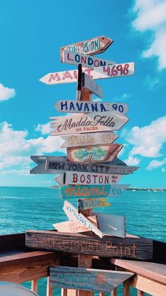 a wooden sign post with many different signs on it's side near the ocean