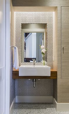 a bathroom sink sitting under a mirror next to a wooden shelf with flowers on it