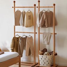 a baby's clothing rack with clothes hanging on it and a bed in the background