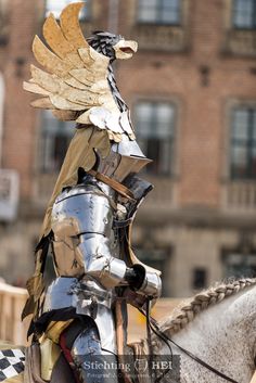 a man in armor riding on the back of a white horse next to a tall building