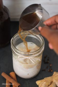 someone pouring ginger syrup into a jar with cinnamon sticks and cloves around it