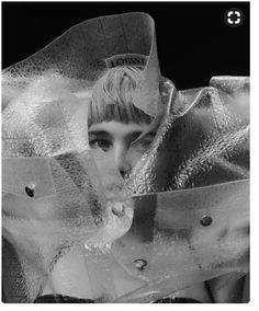 black and white photograph of a woman wearing a hat with ribbons around her neck, looking at the camera