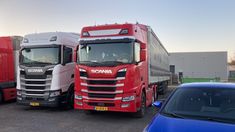 three semi trucks parked next to each other in a parking lot near a blue car