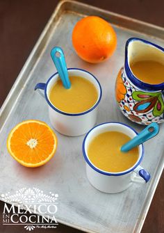 three cups of soup on a tray with oranges