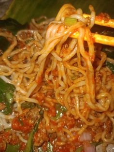 noodles with meat and vegetables are being stirred by chopsticks