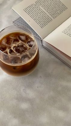 an open book sitting on top of a table next to a glass filled with ice