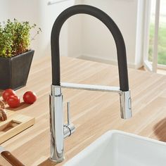 a kitchen sink sitting next to a cutting board with tomatoes on it and a potted plant in the background