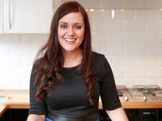 a woman standing in a kitchen wearing a black top and blue skirt with her hands on her hips